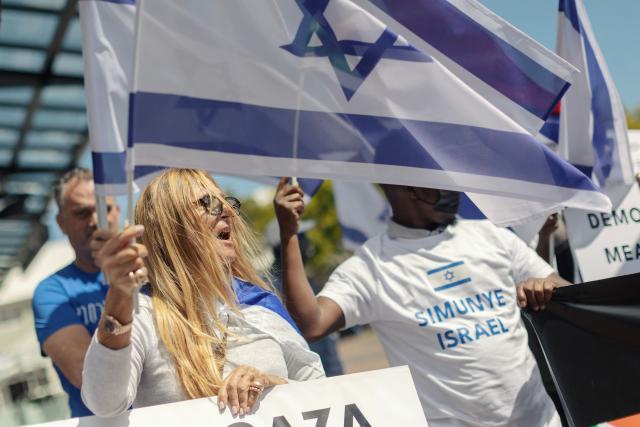 Supporters of Israel chant slogans and hold flags as they take part in a demonstration together with nd Iranian pro-democracy activists on one of the main alley of the Victoria and Albert Waterfront shopping mall in Cape Town, on March 7, 2026. (Photo by GIANLUIGI GUERCIA / AFP)