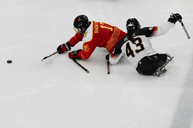 China's Shen Yifeng (L) fights for the puck with Germany's Bernhard Hering during the ice hockey match between China and Germany at the Milano Cortina 2026 Paralympic Winter Games in Milan on March 7, 2026. (Photo by Stefano RELLANDINI / AFP)