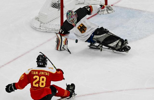 China's Tian Jintao (L) fights for the puck with Germany's goalkeeper Simon Kunst during the ice hockey match between China and Germany at the Milano Cortina 2026 Paralympic Winter Games in Milan on March 7, 2026. (Photo by Stefano RELLANDINI / AFP)
