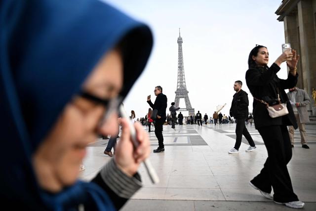 Pedestrians walk past the Eiffel Tower on the Place du Trocadero in Paris on March 7, 2026. (Photo by Lou BENOIST / AFP)