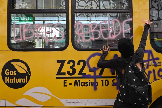 A demonstrator paints graffiti on a bus during a rally on the eve of International Women's Day in Bogota on March 7, 2026. (Photo by Diana SANCHEZ / AFP)
