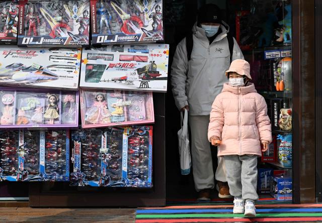 A man and a child walk out of a children's store in Beijing on March 7, 2026. The world's second-most populous country is threatened with a demographic crisis after its birth rate halved over the past decade -- all while people rapidly age out of the workforce. (Photo by Adek BERRY / AFP) / TO GO WITH AFP STORY: China-economy-demographics-infants, by Mary YANG
