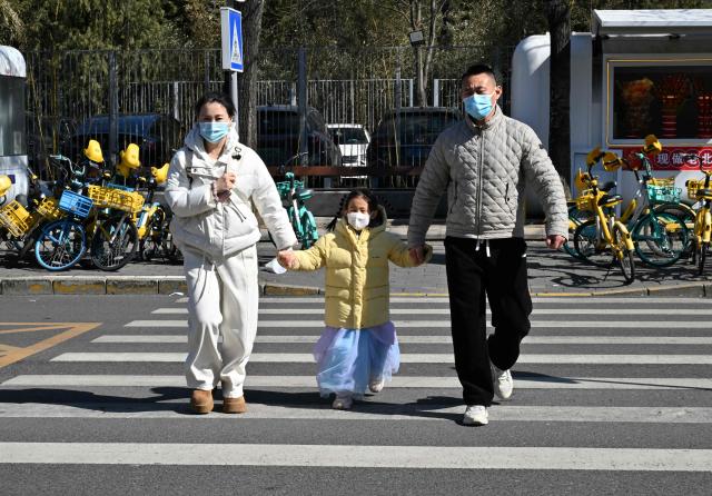A family crosses a road in Beijing on March 6, 2026. The world's second-most populous country is threatened with a demographic crisis after its birth rate halved over the past decade -- all while people rapidly age out of the workforce. (Photo by Adek BERRY / AFP) / TO GO WITH AFP STORY: China-economy-demographics-infants, by Mary YANG