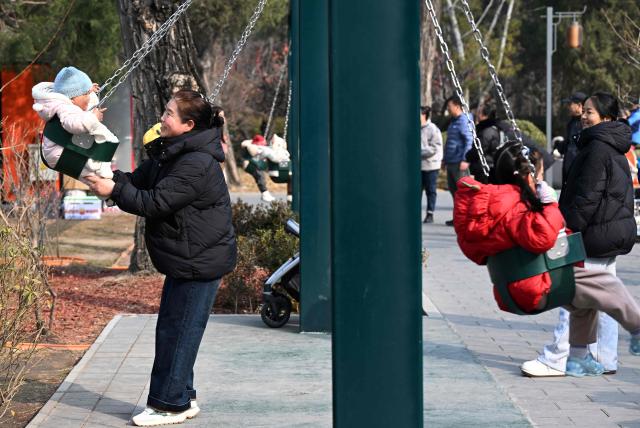 Families play on swings at a park in Beijing on March 7, 2026. The world's second-most populous country is threatened with a demographic crisis after its birth rate halved over the past decade -- all while people rapidly age out of the workforce. (Photo by Adek BERRY / AFP) / TO GO WITH AFP STORY: China-economy-demographics-infants, by Mary YANG