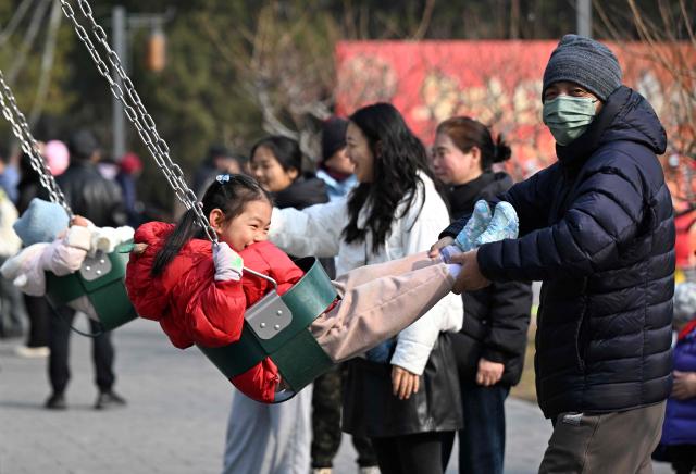 Families play on swings at a park in Beijing on March 7, 2026. The world's second-most populous country is threatened with a demographic crisis after its birth rate halved over the past decade -- all while people rapidly age out of the workforce. (Photo by Adek BERRY / AFP) / TO GO WITH AFP STORY: China-economy-demographics-infants, by Mary YANG