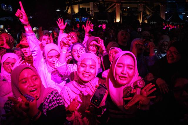 Muslim women react to a performance during the 15th Ramadhan Jazz Festival in the courtyard of the Cut Meutia Mosque, a historic mosque in a converted Dutch colonial building, in Jakarta on March 7, 2026. (Photo by Yasuyoshi Chiba / AFP)