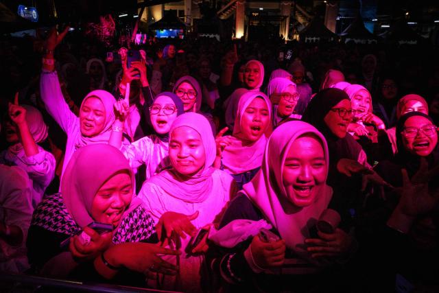 Muslim women react to a performance during the 15th Ramadhan Jazz Festival in the courtyard of the Cut Meutia Mosque, a historic mosque in a converted Dutch colonial building, in Jakarta on March 7, 2026. (Photo by Yasuyoshi Chiba / AFP)