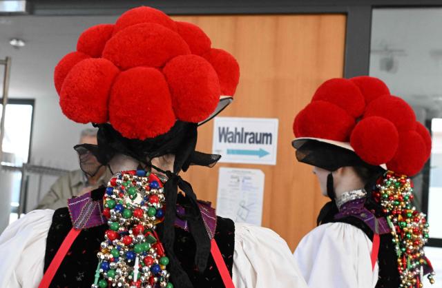 Women wearing a traditional "Bollenhut" pompon hat, typical for the Black Forest region, enter a polling station for the state elections in the federal state of Baden-Wuerttemberg, at a polling station in Gutach, southern Germany, on March 8, 2026. Voters head to the polls in the southwestern state of Baden-Wuerttemberg, a prosperous hub of Germany's flagship auto sector with a population of 11.2 million. (Photo by THOMAS KIENZLE / AFP)