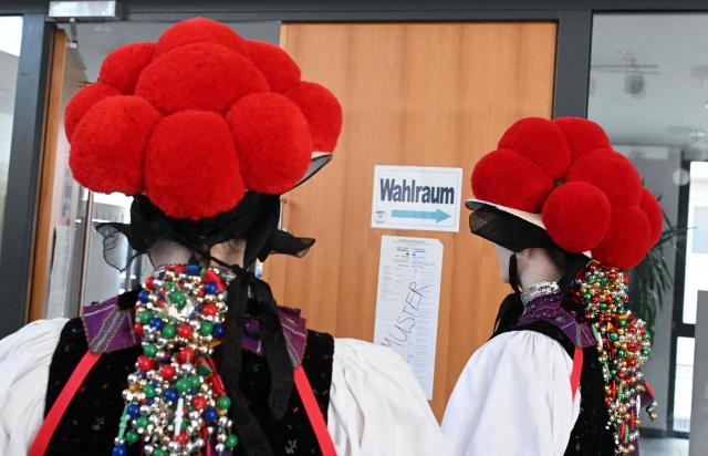 Women wearing a traditional "Bollenhut" pompon hat, typical for the Black Forest region, enter a polling station for the state elections in the federal state of Baden-Wuerttemberg, at a polling station in Gutach, southern Germany, on March 8, 2026. Voters head to the polls in the southwestern state of Baden-Wuerttemberg, a prosperous hub of Germany's flagship auto sector with a population of 11.2 million. (Photo by THOMAS KIENZLE / AFP)