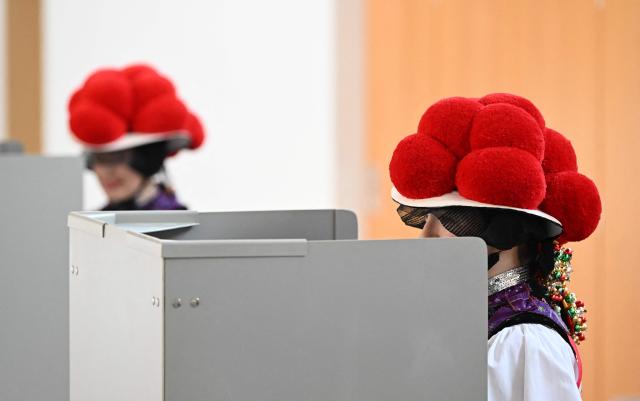 Women wearing traditional "Bollenhut" pompon hats, typical for the Black Forest region, fill out their ballot papers for the state elections in the federal state of Baden-Wuerttemberg, at a polling station in Gutach, southern Germany, on March 8, 2026. Voters head to the polls in the southwestern state of Baden-Wuerttemberg, a prosperous hub of Germany's flagship auto sector with a population of 11.2 million. (Photo by THOMAS KIENZLE / AFP)