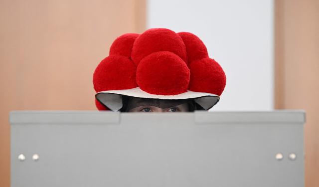 A woman wearing a traditional "Bollenhut" pompon hat, typical for the Black Forest region, fills out her ballot papers for the state elections in the federal state of Baden-Wuerttemberg, at a polling station in Gutach, southern Germany, on March 8, 2026. Voters head to the polls in the southwestern state of Baden-Wuerttemberg, a prosperous hub of Germany's flagship auto sector with a population of 11.2 million. (Photo by THOMAS KIENZLE / AFP)