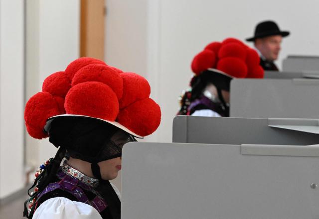 Women wearing traditional "Bollenhut" pompon hats, typical for the Black Forest region, fill out their ballot papers for the state elections in the federal state of Baden-Wuerttemberg, at a polling station in Gutach, southern Germany, on March 8, 2026. Voters head to the polls in the southwestern state of Baden-Wuerttemberg, a prosperous hub of Germany's flagship auto sector with a population of 11.2 million. (Photo by THOMAS KIENZLE / AFP)