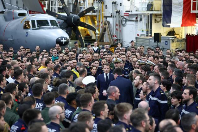 TOPSHOT - French President Emmanuel Macron (C) sings the French national anthem after speaking to the crew as he visits the French aircraft carrier Charles de Gaulle deployed in the Mediterranean Sea following Iranian drone strikes on Cyprus, on March 9, 2026, on the sidelines of his trip to Cyprus to discuss regional security. (Photo by Gonzalo Fuentes / POOL / AFP)