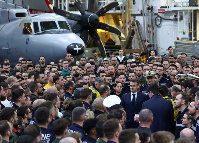 French President Emmanuel Macron (C) stands with the crew as he visits the French aircraft carrier Charles de Gaulle deployed in the Mediterranean Sea following Iranian drone strikes on Cyprus, on March 9, 2026, on the sidelines of his trip to Cyprus to discuss regional security. (Photo by Gonzalo Fuentes / POOL / AFP)