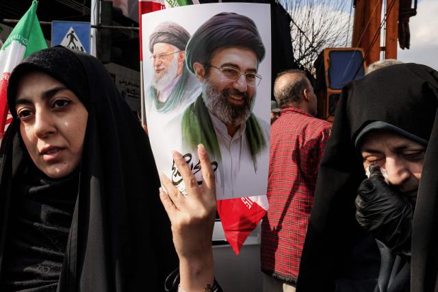 TOPSHOT - A woman holds a poster of Iran's new supreme leader Ayatollah Mojtaba Khamenei (R), next to his late father Ali Khamenei, during a rally in support of him at Enghelab Square in Tehran on March 9, 2026. Iran marked the appointment of Ayatollah Mojtaba Khamenei to replace his father as its supreme leader with a new barrage of missiles against Israel and the Gulf states on March 9, as the Middle East war sent oil prices soaring. (Photo by Atta KENARE / AFP)