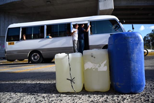 A passenger bus passes by plastic gallons filled with gasoline in Tegucigalpa on March 9, 2026. The prices of petroleum derivatives soared on March 9 in Honduras due to the war in the Middle East. (Photo by Orlando SIERRA / AFP)