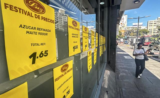 A woman walks in front of price signs on a supermarket window in Caracas on March 9, 2026. Venezuela closed 2025 with the highest inflation in the world: 475%, a brutal acceleration tied to the currency chaos triggered by the tightening of US sanctions against the ousted President Nicolas Maduro. (Photo by Juan BARRETO / AFP)