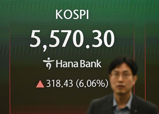 A currency dealer walks past in front of an electronic screen showing South Korea's benchmark stock index (KOSPI) in a foreign exchange dealing room at the Hana Bank headquarters in Seoul on March 10, 2026. Stock markets in South Korea and Japan rose sharply in early trade on March 10, after the US crude oil benchmark, WTI, fell more than six percent. (Photo by Jung Yeon-je / AFP)