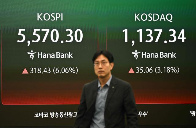 A currency dealer walks past in front of an electronic screen showing South Korea's benchmark stock index (KOSPI) and the Korean Securities Dealers Automated Quotations (KOSDAQ) in a foreign exchange dealing room at the Hana Bank headquarters in Seoul on March 10, 2026. Stock markets in South Korea and Japan rose sharply in early trade on March 10, after the US crude oil benchmark, WTI, fell more than six percent. (Photo by Jung Yeon-je / AFP)