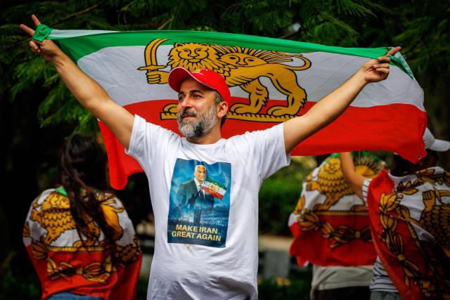 A member of the Iranian community in Australia stands with a pre-revolution Iranian flag with lion and sun emblem while wearing a T-shirt depicting Reza Pahlavi, the son of Iran's late shah, in a show of support outside the Royal Pines Resort, where members of the Iranian womens football team are staying, on the Gold Coast on March 10, 2026. Five players in Iran's visiting women's football team have taken asylum in Australia over fears of persecution at home for not singing the national anthem before a match, the government said on March 10. (Photo by Patrick HAMILTON / AFP)