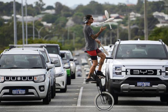 This photo taken on March 9, 2026 shows a street busker juggling while riding a unicycle at a traffic intersection in Perth. (Photo by Antony DICKSON / AFP)