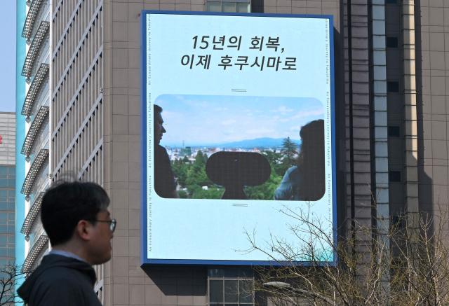 A man walks past a billboard showing a promotional video for tourism in Japan's Fukushima region and reading "15 years of recovery, now to Fukushima", in downtown Seoul on March 10, 2026. A tourism promotion video for Japan's tsunami-hit Fukushima region is being shown on billboards across the South Korean capital Seoul for the first time since the 2011 nuclear accident, a Japanese official said on March 10. (Photo by Jung Yeon-je / AFP)