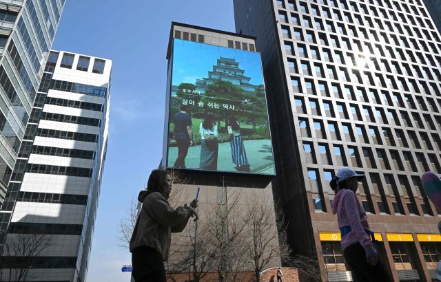 Pedestrians walk past a billboard showing a promotional video for tourism in Japan's Fukushima region, in downtown Seoul on March 10, 2026. A tourism promotion video for Japan's tsunami-hit Fukushima region is being shown on billboards across the South Korean capital Seoul for the first time since the 2011 nuclear accident, a Japanese official said on March 10. (Photo by Jung Yeon-je / AFP)