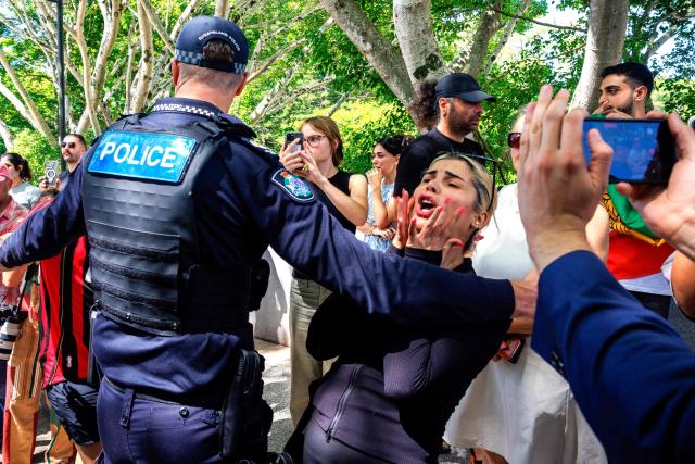 Members of the Iranian community in Australia react as police officers remove them from the path of a departing bus transporting members of the Iranian Women’s Asia Cup football team to the airport, outside the Royal Pines Resort on the Gold Coast on March 10, 2026. Five players from Iran's visting women's football team claimed asylum in Australia on March 10, seeking protection after they were branded "traitors" at home for refusing to sing the national anthem. (Photo by Patrick HAMILTON / AFP)