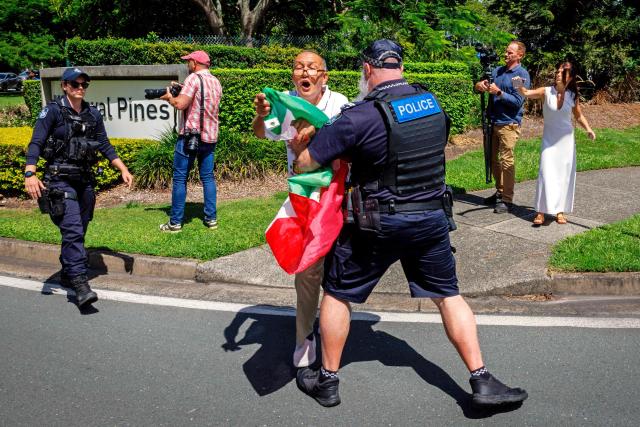 Police officers remove members of the Iranian community in Australia from blocking the path of a departing bus transporting members of the Iranian Women’s Asia Cup football team to the airport, outside the Royal Pines Resort on the Gold Coast on March 10, 2026. Five players in Iran's visiting women's football team have taken asylum in Australia over fears of persecution at home for not singing the national anthem before a match, the government said on March 10. (Photo by Patrick HAMILTON / AFP)