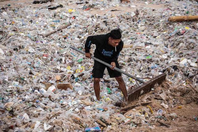 A resident clears marine debris and plastic waste washed ashore during the monsoon season from Jimbaran Beach on Indonesia's resort island of Bali on March 10, 2026. (Photo by Lana Priatna / AFP)