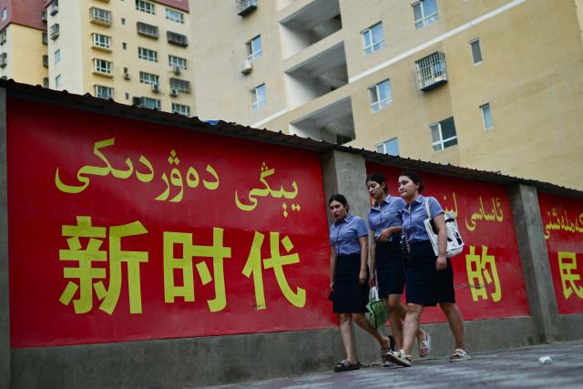 FILE- This picture taken on July 18, 2023, shows women walking past a propaganda slogan promoting ethnic unity in the new era, in both Chinese and Uyghur languages, in Yarkant, northwestern China's Xinjiang region. China's National People's Congress is expected to approve a new "ethnic unity" law during its annual session this week. (Photo by PEDRO PARDO / AFP)