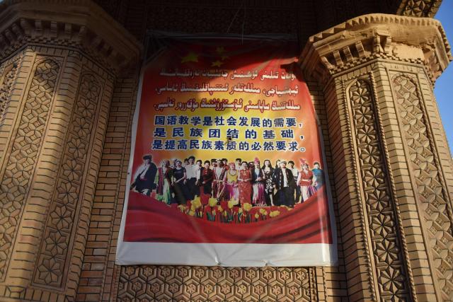 This photo taken on May 31, 2019 shows a poster urging the teaching of Mandarin as the basis for ethnic unity at a bazaar in Hotan, in China's northwest Xinjiang region. China's National People's Congress is expected to approve a new "ethnic unity" law during its annual session this week. (Photo by GREG BAKER / AFP)