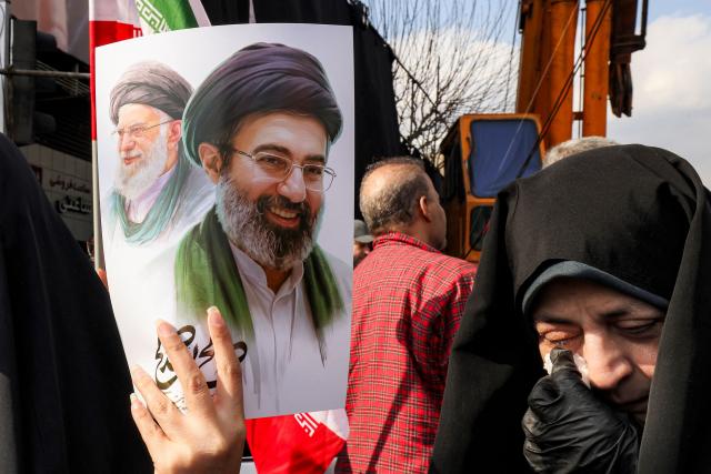 A woman holds a poster of Iran's new supreme leader Ayatollah Mojtaba Khamenei (R), next to his late father Ali Khamenei, during a rally in support of him at Enghelab Square in Tehran on March 9, 2026. Iran marked the appointment of Ayatollah Mojtaba Khamenei to replace his father as its supreme leader with a new barrage of missiles against Israel and the Gulf states on Monday, as the Middle East war sent oil prices soaring. (Photo by Atta KENARE / AFP) / Attention editors: AFP covers the war in the Middle East through its extensive regional network, including bureaus in Tehran, Jerusalem and several neighboring countries.Since the start of the conflict, journalists have been working under increasingly restrictive conditions. Authorities in several countries have limited reporters movements, photo and live video coverage from sensitive locations. Some governments and armed groups have banned images of missile or drone strikes and other security-related sites. / 