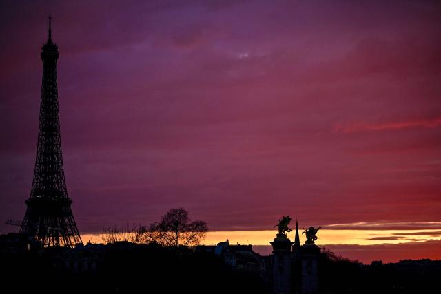 The Eiffel Tower (L), statues of the Pont Alexandre III bridge (R) and the spire of the American Church in Paris (rear) are silhouetted at sunset on March 9, 2026. (Photo by Christophe DELATTRE / AFP)