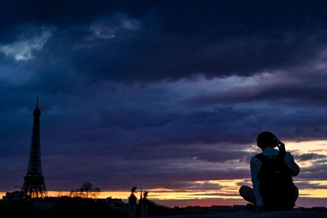 An onlooker sits facing the silhouetted Eiffel Tower at sunset on March 9, 2026. (Photo by Christophe DELATTRE / AFP)