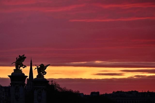Statues of the Pont Alexandre III bridge (R) and the spire of the American Church in Paris (rear) are silhouetted at sunset on March 9, 2026. (Photo by Christophe DELATTRE / AFP)