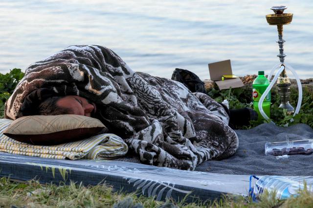 TOPSHOT - A man sleeps under a blanket next to a smoking waterpipe (Shisha or Hookah) in a makeshift encampment along the waterfront in Beirut on March 10, 2026, as civilians who fled the city's southern suburbs due to Israeli bombardment remain displaced. Lebanese authorities said on March 9 that Israel's attacks since March 2 have killed at least 486 people and wounded at least 1,313, with more than 660,000 registered as displaced and 120,000 sleeping at official shelters. Lebanon was drawn into the Middle East war when Iran-backed Hezbollah attacked Israel, in response to the killing of the Iranian supreme leader in US-Israeli strikes on February 28. (Photo by Anwar AMRO / AFP) / Attention editors: AFP covers the war in the Middle East through its extensive regional network, including bureaus in Tehran, Jerusalem and several neighboring countries.Since the start of the conflict, journalists have been working under increasingly restrictive conditions. Authorities in several countries have limited reporters movements, photo and live video coverage from sensitive locations. Some governments and armed groups have banned images of missile or drone strikes and other security-related sites. / 