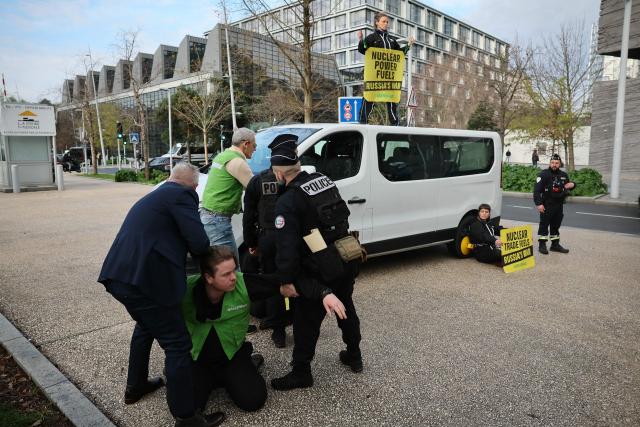 Police officers detain activists during a Greenpeace action to protest against the Nuclear Energy Summit at the Seine Musicale performing arts center in Boulogne-Billancourt outside Paris on March 10, 2026. (Photo by Dimitar DILKOFF / AFP)