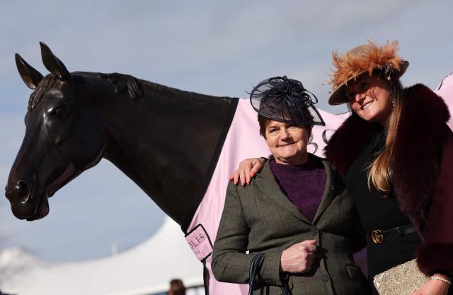 Racegoers pose for a photograph with a statue of Best Mate, ahead of racing on the first day of the Cheltenham Festival at Cheltenham Racecourse, in Cheltenham, western England on March 10, 2026. (Photo by Adrian Dennis / AFP)