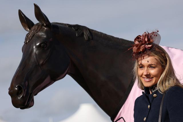 A racegoer poses for a photograph with a statue of Best Mate, ahead of racing on the first day of the Cheltenham Festival at Cheltenham Racecourse, in Cheltenham, western England on March 10, 2026. (Photo by Adrian Dennis / AFP)