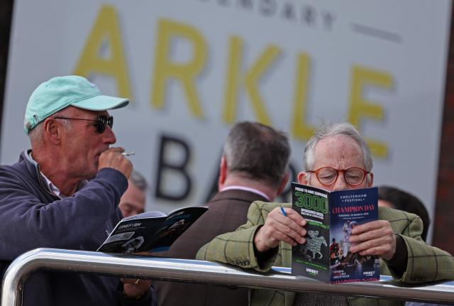 Racegoers study the form guide ahead of racing on the first day of the Cheltenham Festival at Cheltenham Racecourse, in Cheltenham, western England on March 10, 2026. (Photo by Adrian Dennis / AFP)