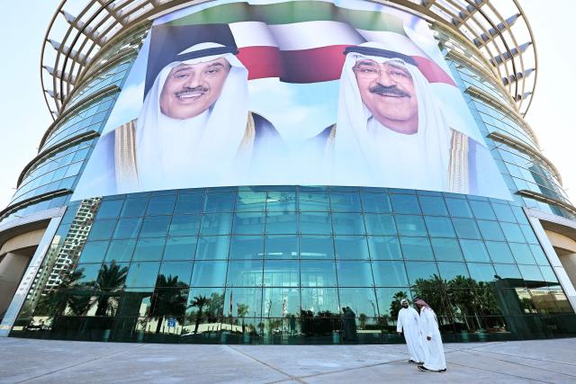 Kuwaiti citizens walk past large portraits of Kuwait's Emir, Sheikh Meshal al-Ahmad al-Sabah (R) and Kuwait's Crown Prince, Sheikh Sabah al-Khaled al-Hamad al-Sabah, displayed on the facade of the Dasman Diabetes Institute building in Kuwait City on March 10, 2026. (Photo by YASSER AL-ZAYYAT / AFP) / Attention editors: AFP covers the war in the Middle East through its extensive regional network, including bureaus in Tehran, Jerusalem, and several neighboring countries. Since the start of the conflict, journalists have been working under increasingly restrictive conditions. Authorities in several countries have limited reporters' movements, photo and live video coverage from sensitive locations. Some governments and armed groups have banned images of missile or drone strikes and other security-related sites. / 