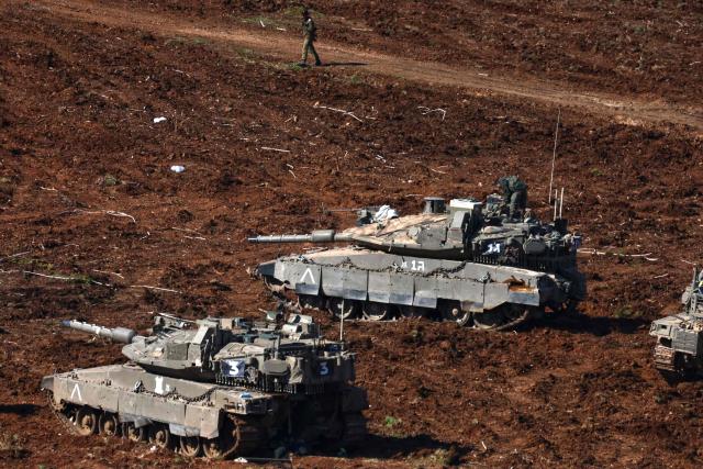 An Israeli army soldier walks near main battle tanks deployed at a position in the upper Galilee in northern Israel near the Lebanon border on March 10, 2026. A strike hit Beirut's southern suburbs on March 10, state media reported, after the Israeli military renewed its warning for people to evacuate the area. Israel's military began striking southern Lebanon on March 4 after issuing a call to evacuate all areas south of the country's Litani river. Lebanon was drawn into the Middle East war when Iran-backed militant group Hezbollah attacked Israel in response to the killing of Iranian supreme leader during US-Israeli strikes. (Photo by AHMAD GHARABLI / AFP) / Attention editors: AFP covers the war in the Middle East through its extensive regional network, including bureaus in Tehran, Jerusalem and several neighboring countries.Since the start of the conflict, journalists have been working under increasingly restrictive conditions. Authorities in several countries have limited reporters movements, photo and live video coverage from sensitive locations. Some governments and armed groups have banned images of missile or drone strikes and other security-related sites. / 