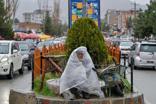 TOPSHOT - An Afghan worker covers himself with a plastic sheet as it rains in the Faizabad district of Badakhshan province on March 10, 2026. (Photo by Omer ABRAR / AFP)
