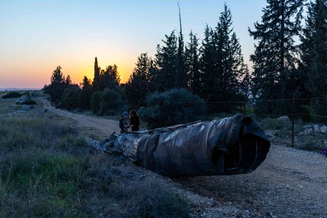 People stand next to a fragment of an Iranian missile on the outskirts of Israel's central city of Elad on March 10, 2026. While Israel's state-of-the-art air defences have managed to largely protect the country from Iran's barrages, Tel Aviv has been repeatedly targeted. (Photo by Ilia YEFIMOVICH / AFP) / Attention editors: AFP covers the war in the Middle East through its extensive regional network, including bureaus in Tehran, Jerusalem and several neighboring countries.Since the start of the conflict, journalists have been working under increasingly restrictive conditions. Authorities in several countries have limited reporters movements, photo and live video coverage from sensitive locations. Some governments and armed groups have banned images of missile or drone strikes and other security-related sites. / 