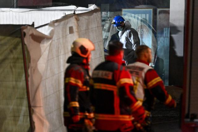 Firefighters and a forensic officer work in a cordoned-off area next to the front of a bus that caught fire, killing at least six people and injuring five others in what police said may have been a deliberate act, in the town of Kerzers, western Switzerland, on March 10, 2026. A bus caught fire in western Switzerland on March 10 killing at least six people and injuring five others in what police said may have been a deliberate act. The fire broke out on the bus in the main street of the small town of Kerzers, around 20 kilometres (12 miles) west of the Swiss capital Bern, at about 6:25 pm (1725 GMT). (Photo by Fabrice COFFRINI / AFP)