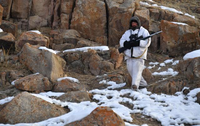 Shepherd Amantur Akmatov, 30, the youngest of the three-generation Akmatov family of white yaks breeders, walks with a hunting rifle during a morning wolf patrol at a high-altitude  white yaks snowy pasture in the remote Kyrgyz mountains on February 3, 2026. (Photo by Vyacheslav OSELEDKO / AFP)