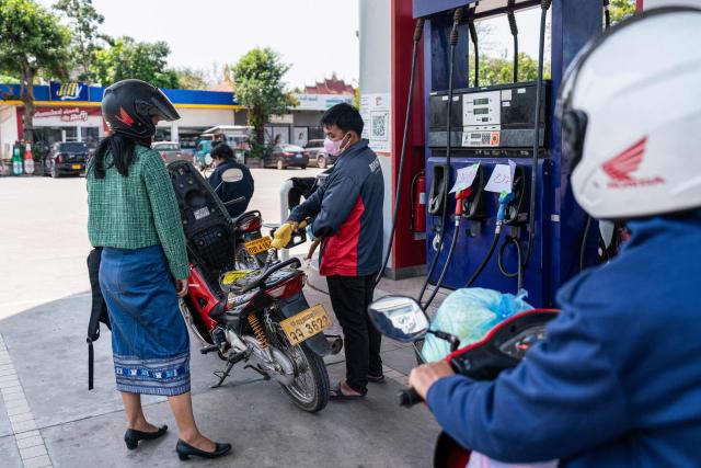 An employee fills the tank of a motorcycle at a gas station in the Donkoi district of Vientiane on March 10, 2026, amid rising petrol prices. The spike in oil prices caused by the war in the Middle East has provoked anxiety in many drivers across Asia. (Photo by AFP)
