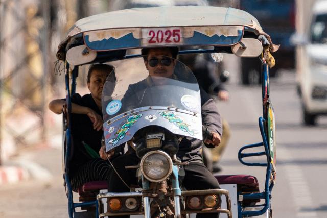 A tuk tuk rider transports a passenger along Kaysone Avenue in Vientiane on March 10, 2026. (Photo by AFP)