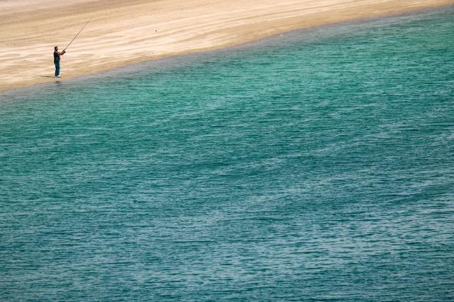A man fishes on the beach in Dubai on March 11, 2026. The Gulf countries have long been seen as islands of stability in the Middle East, but the war in the region could threaten their prosperity, analysts said, pointing to risks to their revenues and reputations as business havens. (Photo by FADEL SENNA / AFP) / Attention editors: AFP covers the war in the Middle East through its extensive regional network, including bureaus in Tehran, Jerusalem, and several neighboring countries. Since the start of the conflict, journalists have been working under increasingly restrictive conditions. Authorities in several countries have limited reporters' movements, photo and live video coverage from sensitive locations. Some governments and armed groups have banned images of missile or drone strikes and other security-related sites. / 